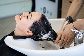 Haircare procedure in beauty salon. Hairdresser is brushing woman`s hair spreading a treatment mask or conditioner