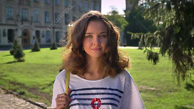 Portrait of a young smiling caucasian brunette in the park, university in the background