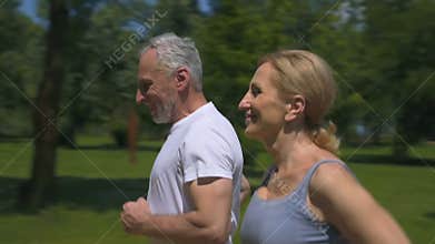 Mature emotional couple jogging in park, active and full of energy, slow-mo
