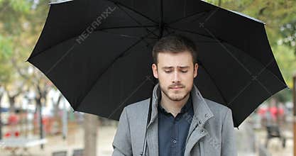 Melancholic man walking in a park a rainy day