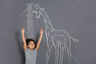 African-American child measuring height near chalk giraffe drawing on grey