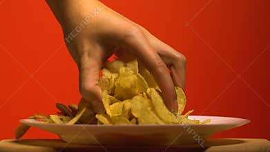 Womans hand grabbing chips from plate, home party with junk food, slow motion