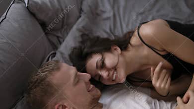 Young playful romantic lovers having fun and tickling on the bed at home or hotel. Then kissing and hugging.Wearing