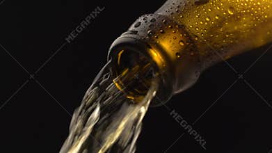Beer pouring into glass from brown bottle in slow motion on black background