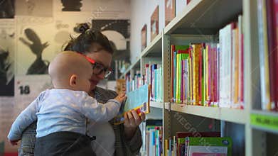 Close portrait of a mother with a baby in her arms near the bookcase in the library. Maternity leave, earlier