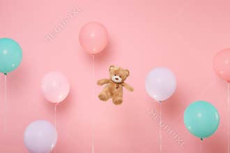 Teddy bear plush toy on pastel bright trending pink background with colorful air balloons. Decoration for birthday