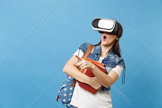 Young shocked woman student with opened mouth with backpack in virtual reality glasses hold school books pointing index