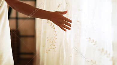 Female hand touching white curtains in cozy bedroom. Young woman wrapped in bath towel in bedroom interior. House design