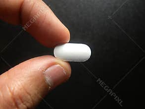 Hand holding white oblong medicine tablet