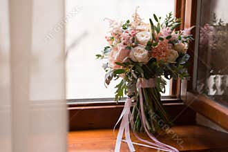Pink and peach wedding bouquet stands on the windowsill