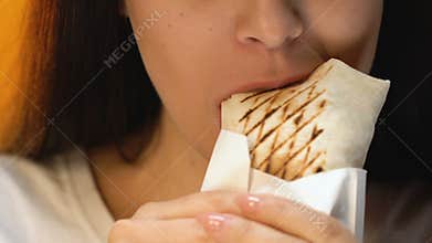Young woman eating tasty chicken roll, unhealthy fast food, appetite, close up