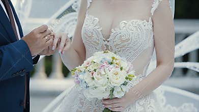 The groom puts the wedding ring on finger of the bride and kisses her hand. The bride and groom exchange wedding rings.