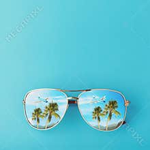 Sunglasses with palm trees, a plane and mountains reflected in them. Concept on the theme of vacation and travel with copy space