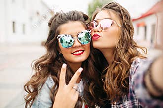 Gorgeous brunette girlfriends with hairstyle, mirrored sunglasses and red lips making selfie with duck face.