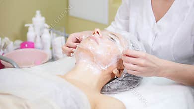 Cosmetologist wraping in film client`s cheeks doing osmetic procedures cleaning of the face in cosmetology clinic.