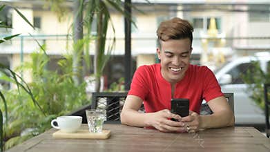 Happy young Asian man using phone at the coffee shop outdoors