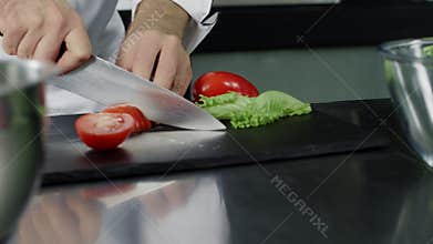 Chef cooking fresh salad at kitchen. Closeup chef hands cutting tomato.