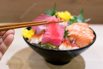 Chopsticks with Tuna sashimi with Mixed sliced fish sashimi on ice in black bowl. Sashimi Salmon Tuna Hamachi Prawn and Surf Calm