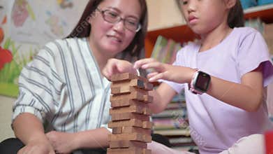 Young mother and her daughter try to build wooden block tower.