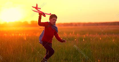 The boy runs across the field with a plane in his hands at sunset
