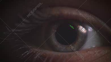 Close-up shoot of gray eye blinking with reflection of green lamp on it in complete darkness.