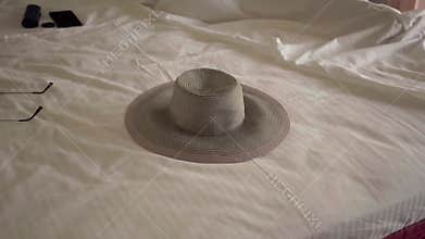 The hat lying on the bed in hotel room. Unrecognizable woman sleeping in the background in a comfortable bed. Tourism