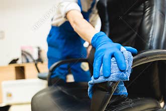 Young man in workwear and rubber gloves cleans the office chair with professional equipment.