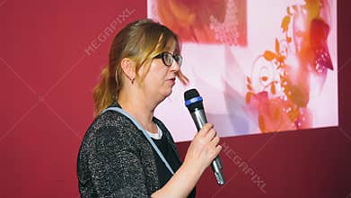Adult woman holding microphone and speaking on performance stage at event