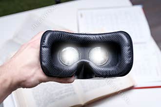 Virtual reality helmet in a man`s hand over books, e-learning, modern technology