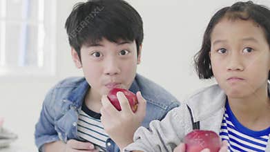 Portrait of young asian boy and little girl eating an apple and looking at camera with smile face