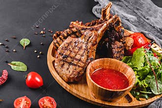 Grilled Ribeye Steak on bone and vegetables with fresh salad and bbq sauce on cutting board over black stone background. Hot Meat