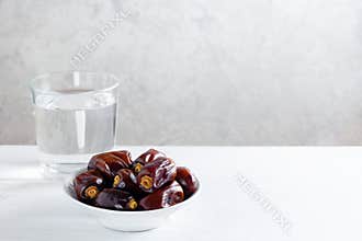 Dates and a glass of water on white wooden table.