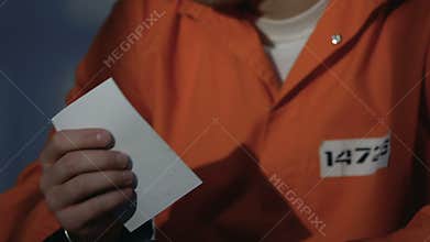 Upset prisoner in handcuffs holding cross and praying to God, asking forgiveness