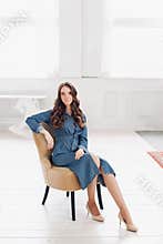 Elegant gorgeous brunette woman in denim dress and heels reading a magazine.