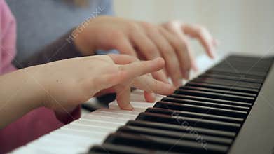 Young woman teaches little girl to play the piano.
