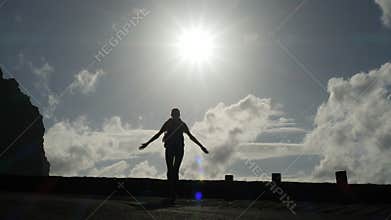 Camera follows a woman silhouette walking out from tunnel towards the sunlight. Burst of bright light. Raising arms in