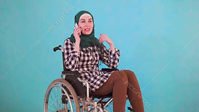 Young Muslim woman disabled in a wheelchair talking on the phone on a blue background
