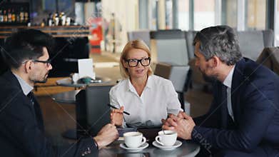 Cheerful business lady negotiating agreement with male partners meeting in cafe