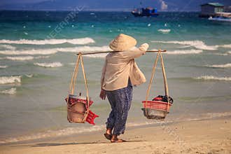 Closeup Vendor Woman with Yoke Walks along Beach against Sea