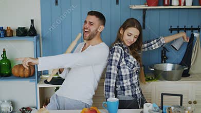 Young joyful couple have fun dancing and singing while set the table for breakfast in the kitchen at home