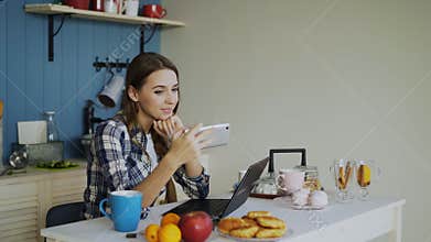 Cheerful smiling woamn talking online video chat using smartphone in the kitchen at home