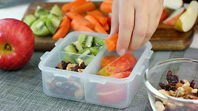 Woman hand put healthy fruit and nut snacks into the lunch box