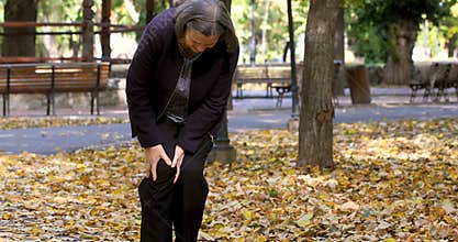 Senior woman having knee pain walking in park
