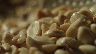 Peeled peanuts are fried in a pan. Hand with a spoon stirring nuts