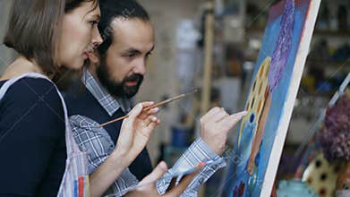 Skilled artist teacher showing and discussing basics of painting to student at art-class