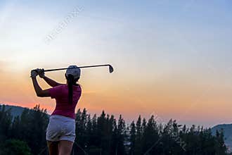 Asian woman Golf player hit swing shot golf ball on the green sunset of green club in evening time.
