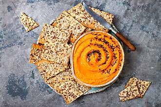 Pumpkin hummus seasoned with olive oil and black sesame seeds with whole grain crackers. Healthy vegetarian appetizer or snack.