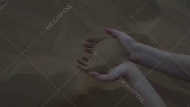 Beautiful women`s hands touch the sand, the sand flutters in the wind.