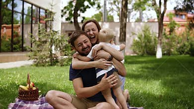 Happy family of three. Parents in casual are sitting on a plaid with opened hands and smiling to their little son. Child
