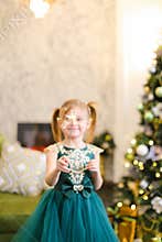 Little female kid wearing dress and standing with bengal lights near Christmas tree.